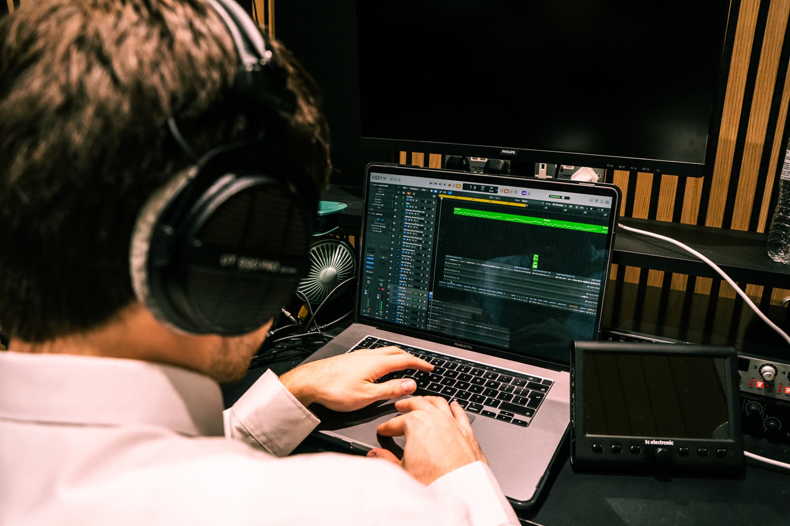 A producer arranging a session in a DAW, shot over the shoulder